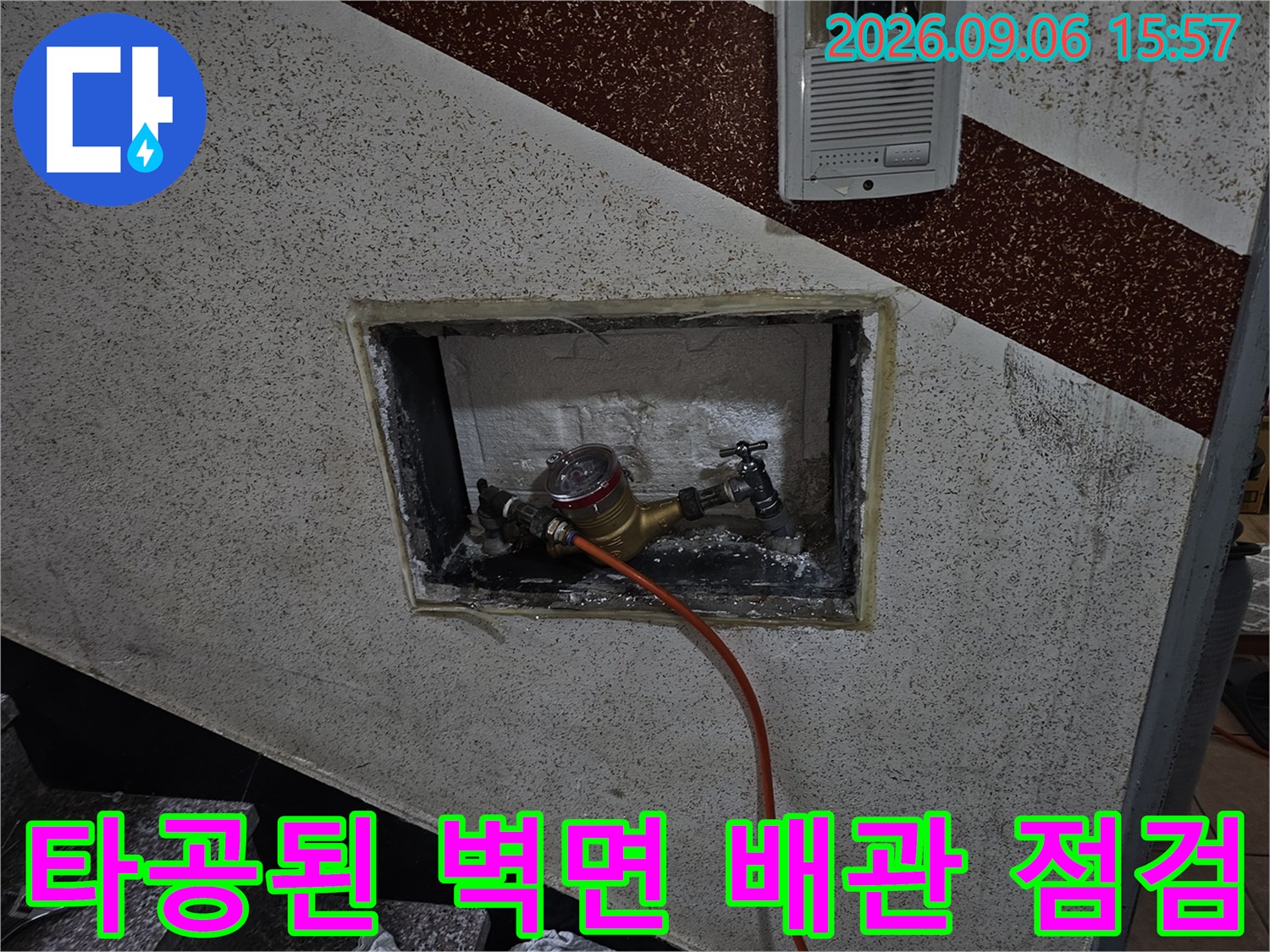 벽면 타공 부위-노출된 배관에 압력계와 주황색 호스가 연결된 모습