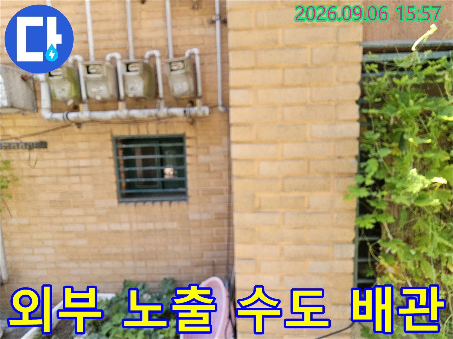 황토색 벽돌 건물에 설치된 외부 수도 계량기 및 수직 연결 관
