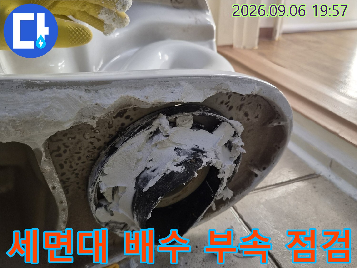 탈거된 세면대 하단부의 검은색 배수 부속과 주변 타일 상태