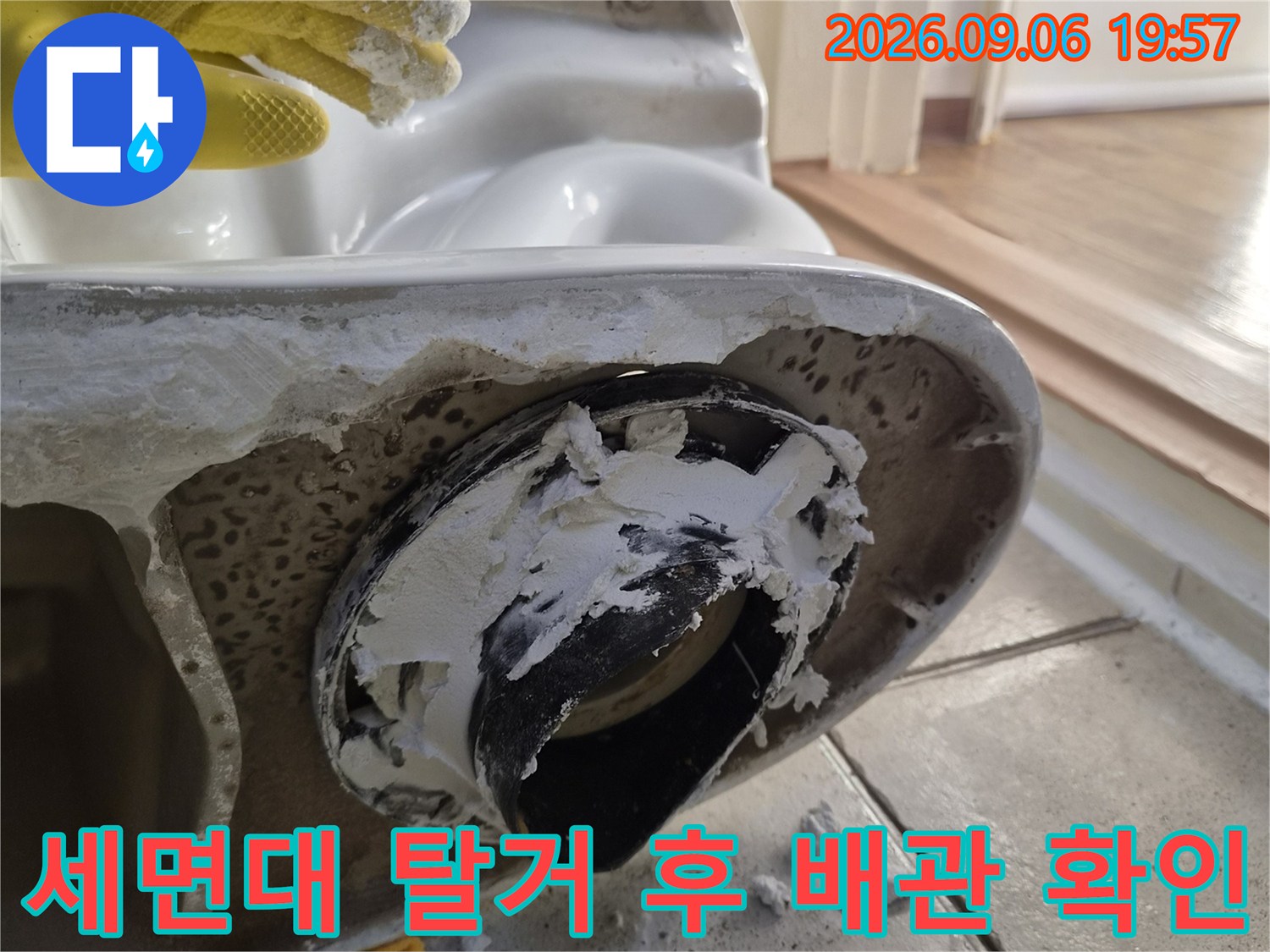 탈거된 세면대 하단에 노출된 검은색 배수 부속과 주변 타일의 상태입니다.