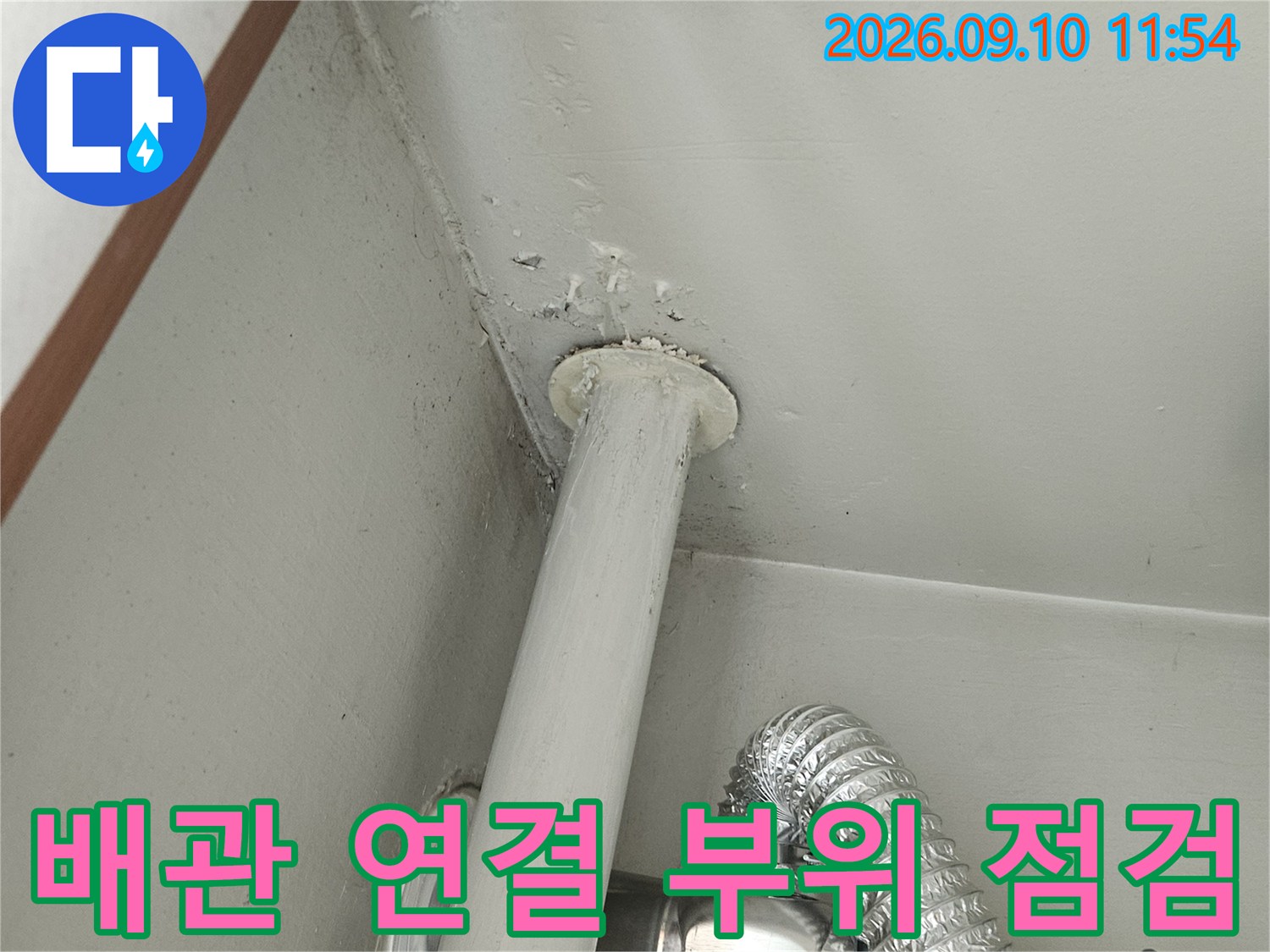 벽을 통과하는 흰색 배관과 은색 배관의 접합 부위 근접 사진