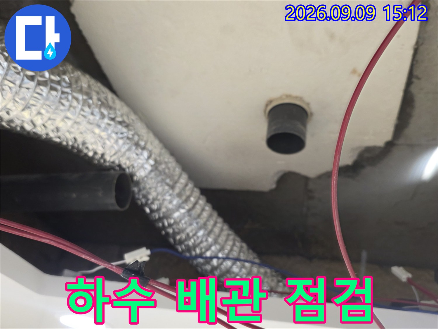 은박 보온재로 감싸진 배관과 검은색 하수 배관이 있는 천장 내부