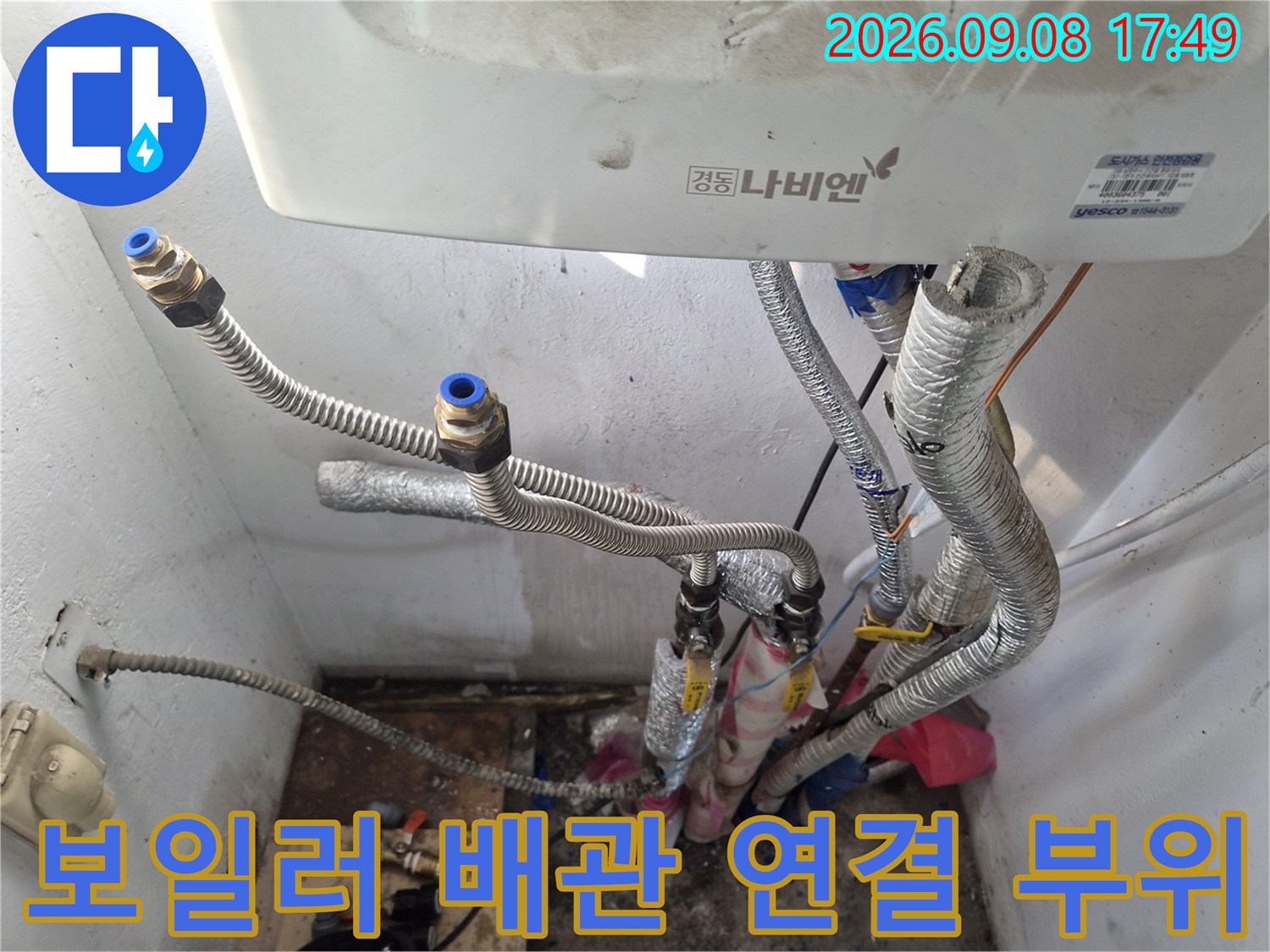 보일러 하단에 연결된 금속 소재의 급수 및 온수 배관 모습