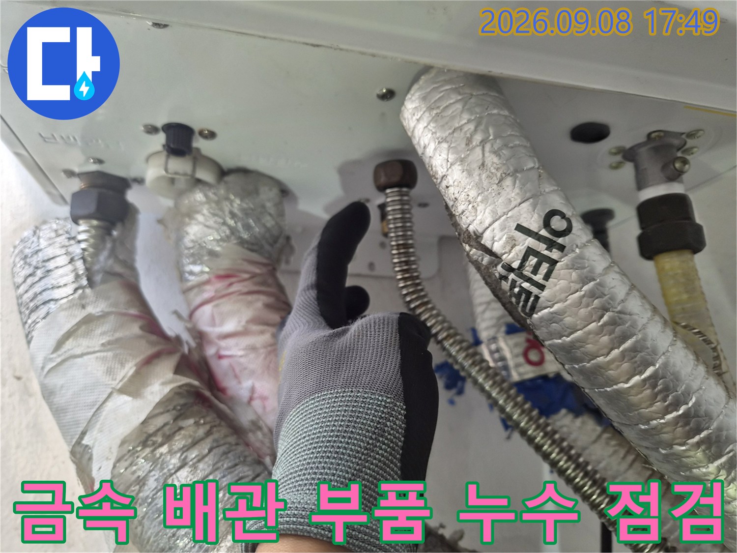 장갑을 낀 작업자가 보일러 하단 금속 연결 부위를 확인하고 있습니다.
