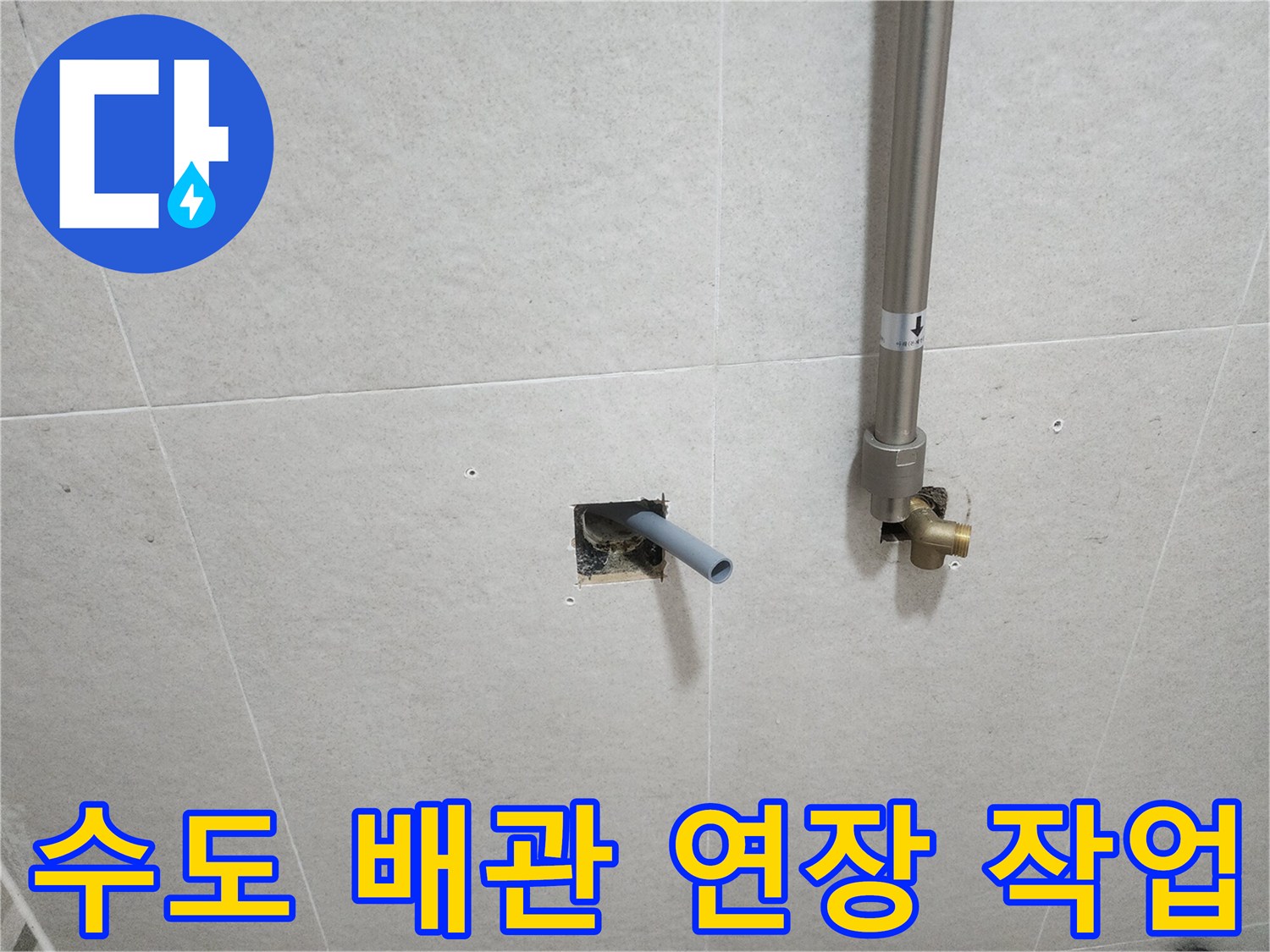타일 벽면 사이로 나온 은색 배관과 연결 부속의 모습