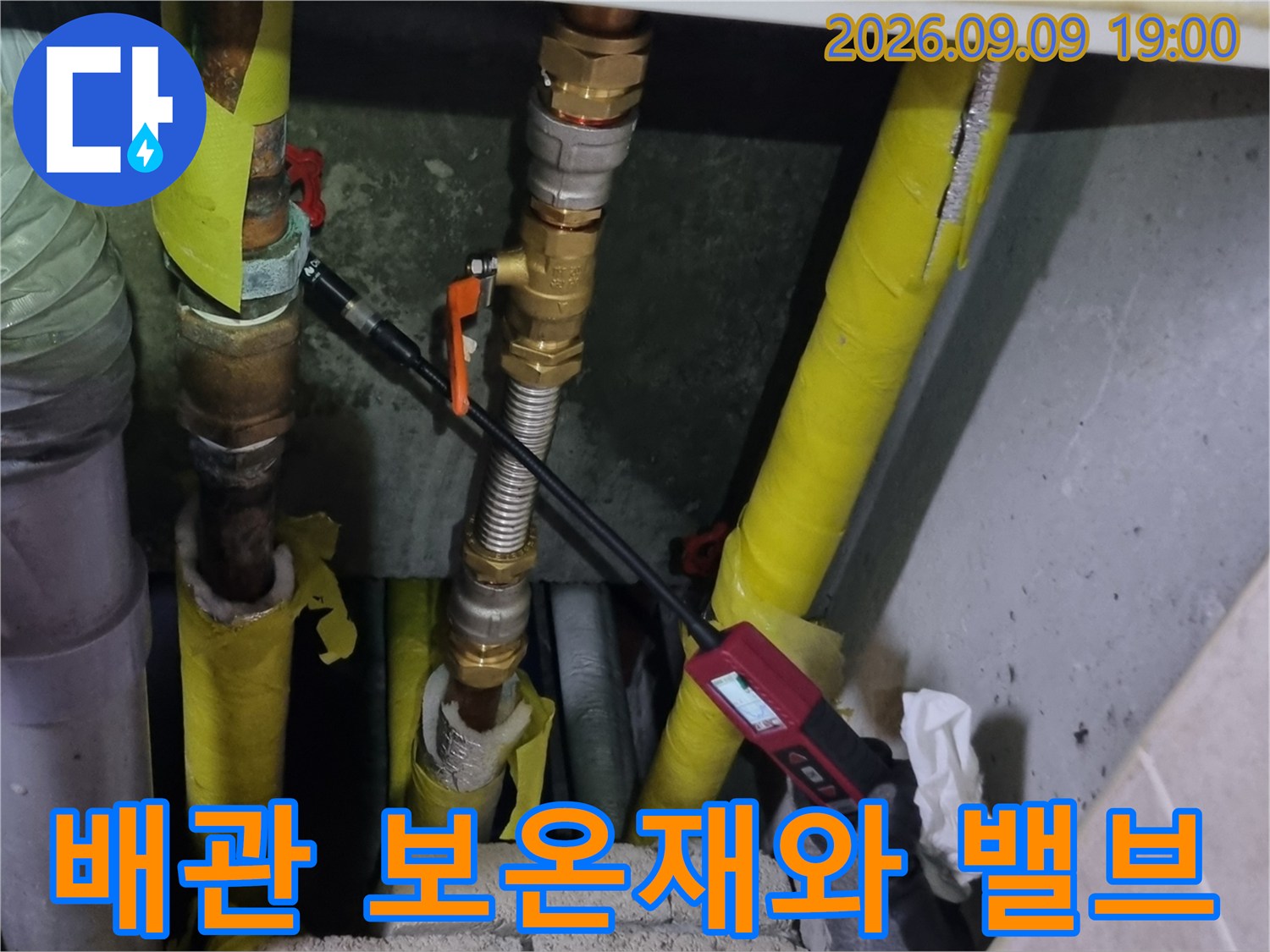 노란색-보온재가 씌워진 배관과 주황색 밸브의 연결부를 보여주는 사진입니다.