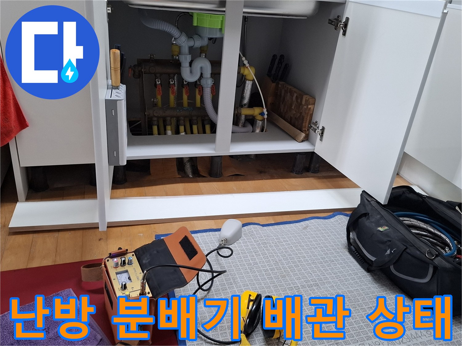싱크대 하부 공간에 노출된 난방 분배기와 각종 연결 배관들의 모습