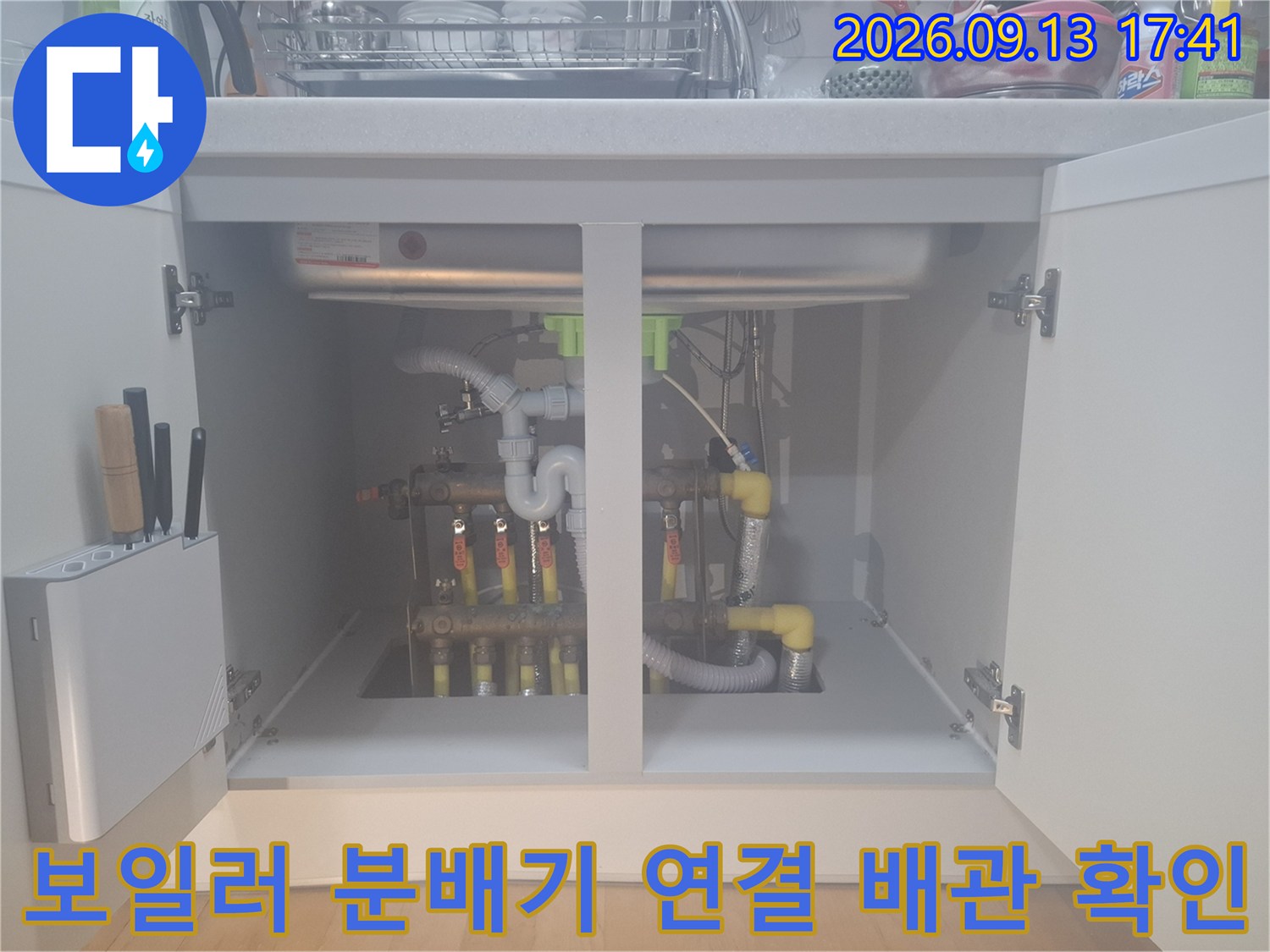 싱크대 하부장에 노출된 보일러 분배기와 다수의 배관 연결 부위 사진입니다.