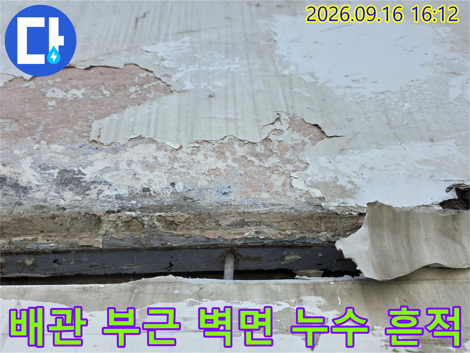 하얀색 배관 연결 부위 주변의 벽면 마감재가 훼손된 현장 사진입니다.
